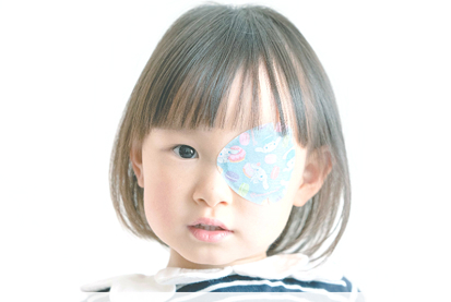 弱視や斜視の訓練のために、片方の目に可愛い柄のアイパッチを着用している子どもの写真。
